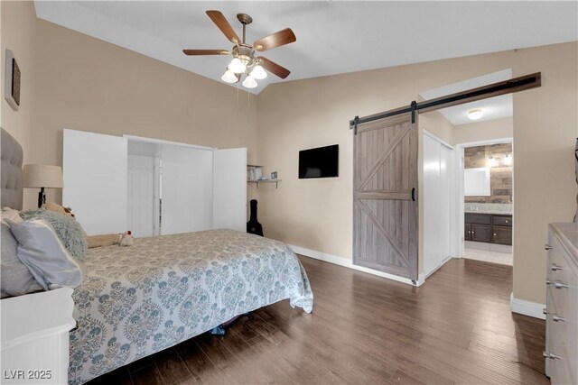 bedroom featuring ensuite bathroom, a barn door, ceiling fan, dark hardwood / wood-style floors, and vaulted ceiling