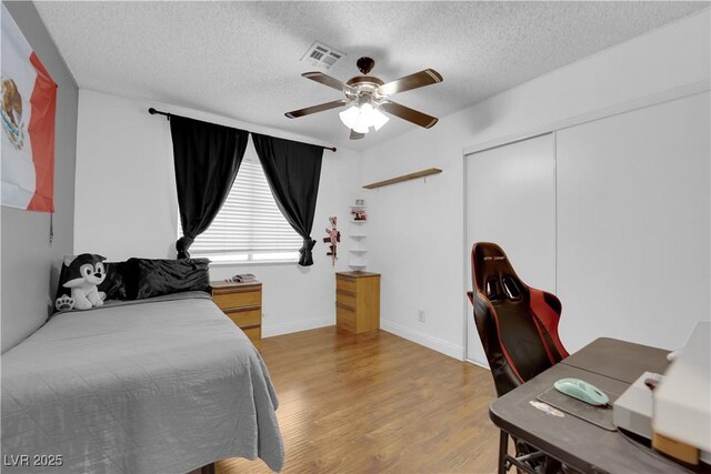 bedroom with ceiling fan, light hardwood / wood-style floors, a textured ceiling, and a closet