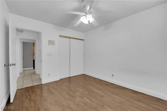 unfurnished bedroom featuring ceiling fan, a closet, a textured ceiling, and light hardwood / wood-style flooring