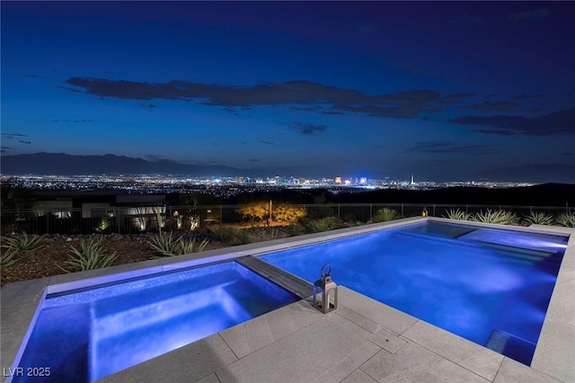 pool at night featuring an in ground hot tub