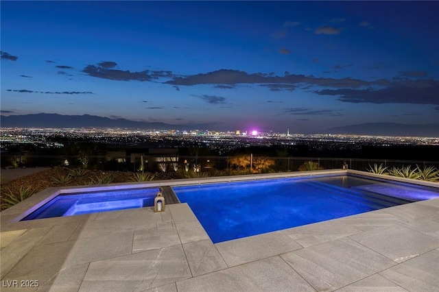 pool at dusk featuring a mountain view and an in ground hot tub