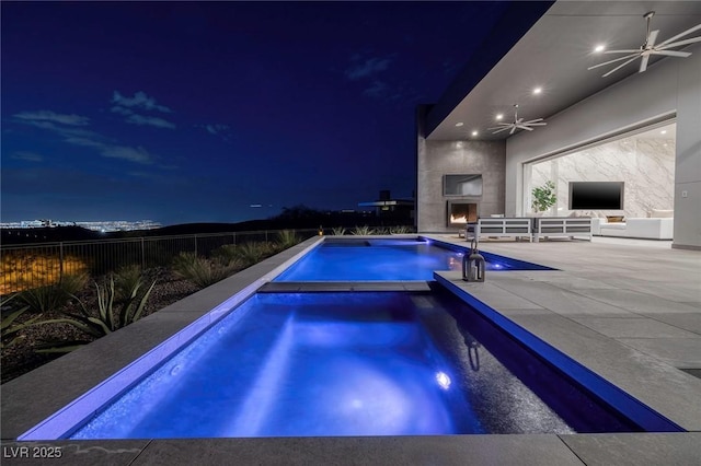 pool at twilight with ceiling fan, a patio, and exterior fireplace