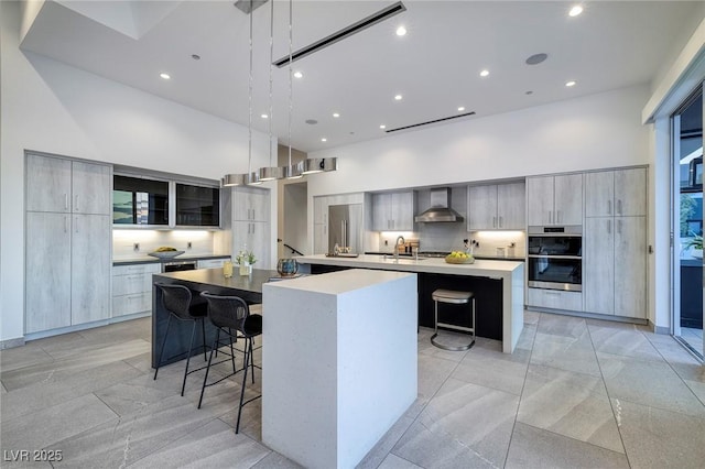 kitchen with a kitchen bar, a high ceiling, a spacious island, wall chimney range hood, and pendant lighting