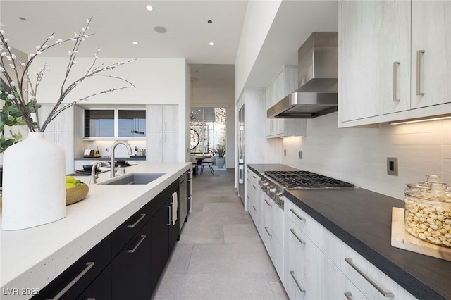 kitchen featuring appliances with stainless steel finishes, wall chimney exhaust hood, white cabinetry, sink, and backsplash