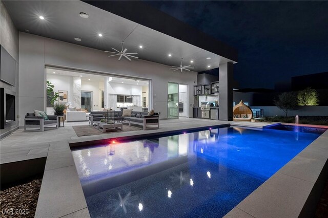 pool at night with ceiling fan, an outdoor hangout area, exterior kitchen, and a patio area