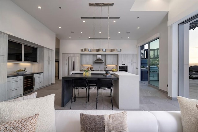 kitchen featuring a large island with sink, gray cabinets, oven, a kitchen bar, and beverage cooler