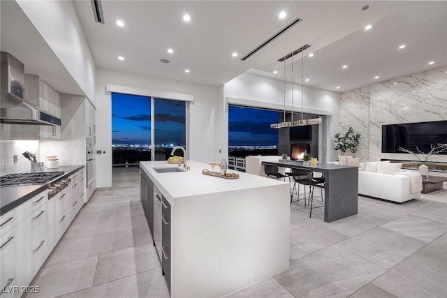 kitchen featuring pendant lighting, sink, stainless steel gas cooktop, a large island, and wall chimney exhaust hood