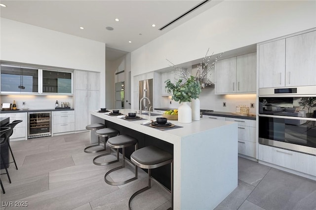 kitchen featuring appliances with stainless steel finishes, tasteful backsplash, a kitchen island with sink, a kitchen breakfast bar, and beverage cooler