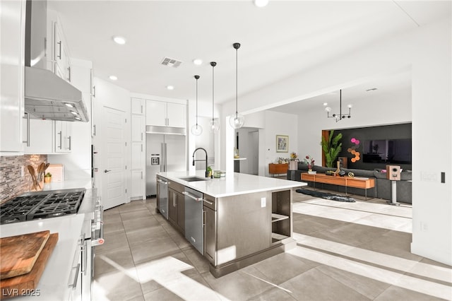 kitchen with white cabinetry, stainless steel appliances, an island with sink, sink, and a notable chandelier