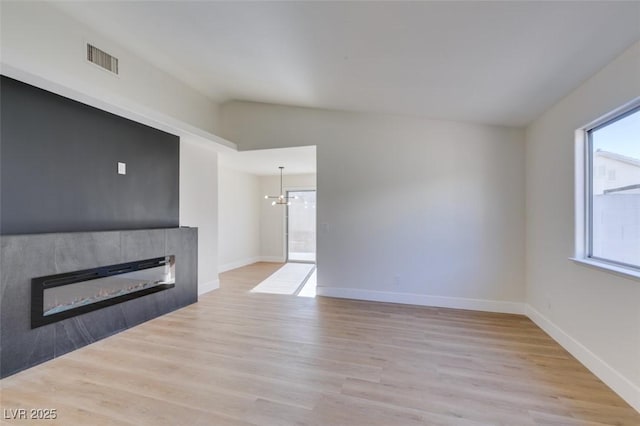 unfurnished living room with a chandelier, a healthy amount of sunlight, light hardwood / wood-style floors, and a tile fireplace