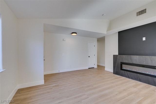 unfurnished living room featuring light hardwood / wood-style floors, lofted ceiling, and a tiled fireplace