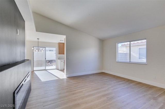 unfurnished living room featuring light hardwood / wood-style flooring, lofted ceiling, and an inviting chandelier