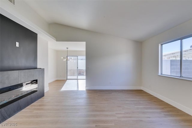 unfurnished living room featuring light hardwood / wood-style flooring, lofted ceiling, and an inviting chandelier