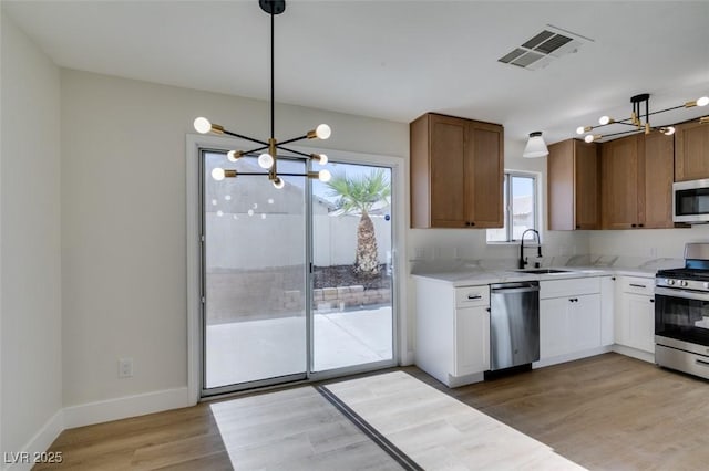 kitchen featuring an inviting chandelier, white cabinetry, stainless steel appliances, pendant lighting, and sink