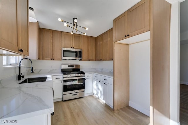 kitchen with stainless steel appliances, white cabinets, light hardwood / wood-style flooring, light stone counters, and sink