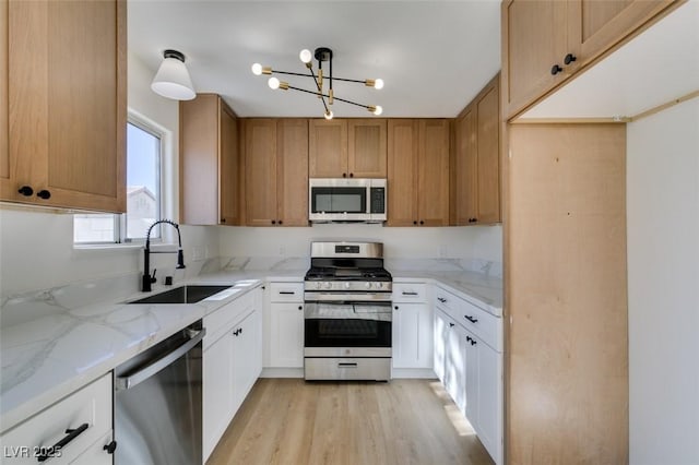 kitchen featuring appliances with stainless steel finishes, white cabinetry, light stone counters, and sink