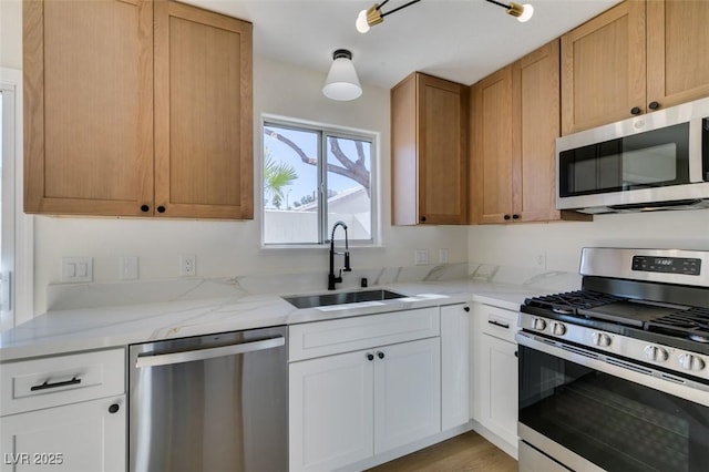 kitchen with sink, white cabinetry, light hardwood / wood-style flooring, stainless steel appliances, and light stone counters