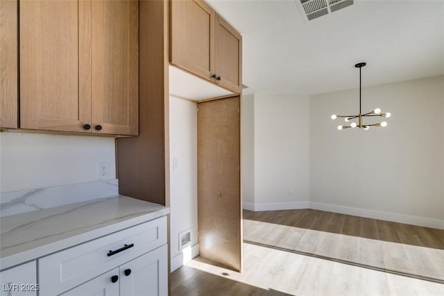 kitchen with a notable chandelier, dark wood-type flooring, white cabinets, hanging light fixtures, and light stone counters