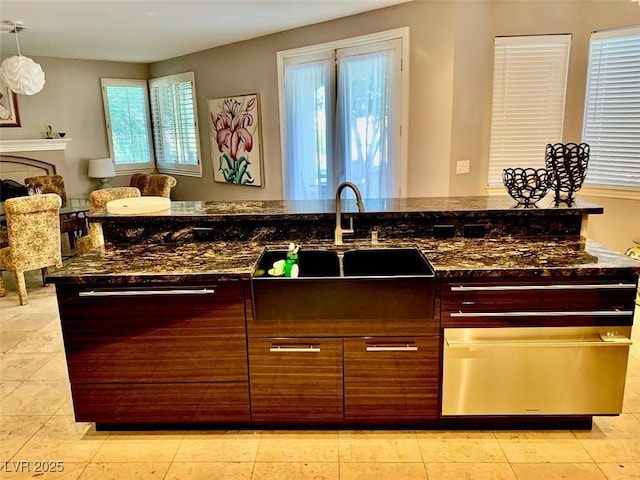 kitchen featuring hanging light fixtures, a wealth of natural light, dark stone counters, and sink