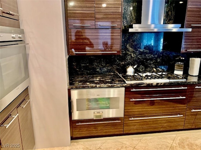 kitchen featuring stainless steel oven, wall chimney range hood, dark stone countertops, and gas stovetop