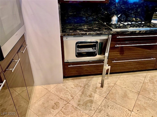 kitchen with light tile patterned floors, decorative backsplash, gas stovetop, dark stone counters, and oven