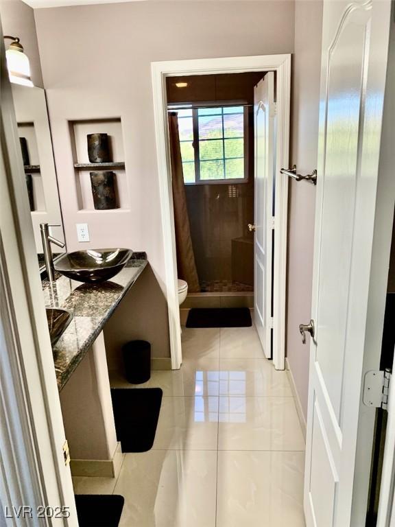 bathroom with toilet, tile patterned flooring, a tile shower, and vanity