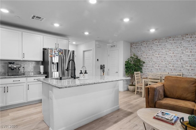 kitchen with a kitchen island with sink, light stone countertops, and stainless steel fridge with ice dispenser