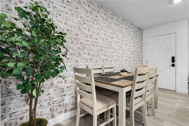 unfurnished dining area featuring brick wall and light hardwood / wood-style flooring