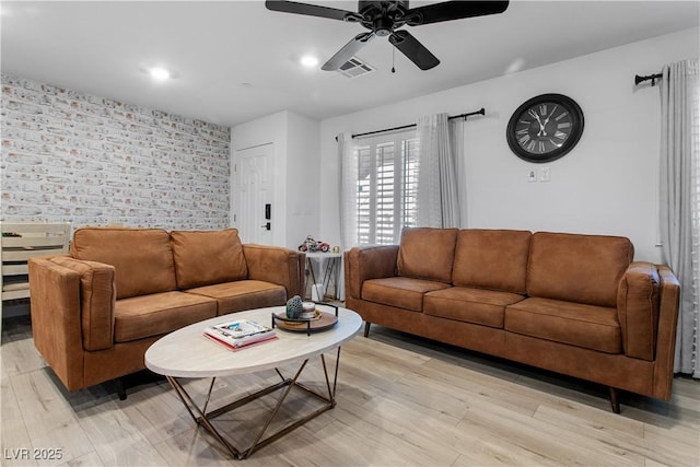 living room with light wood-type flooring, ceiling fan, and brick wall