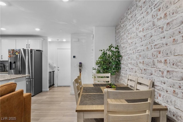 dining space with brick wall and light hardwood / wood-style flooring