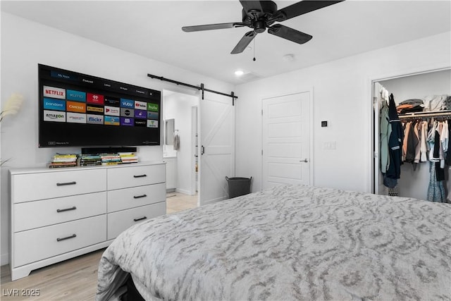 bedroom featuring ceiling fan, a barn door, connected bathroom, a walk in closet, and a closet