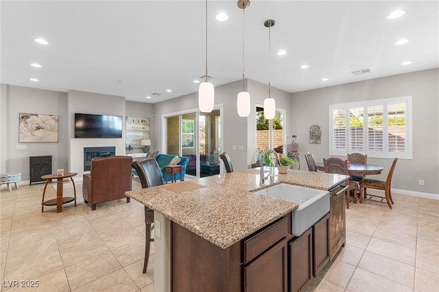 kitchen featuring dark brown cabinetry, decorative light fixtures, sink, a kitchen island with sink, and light stone counters