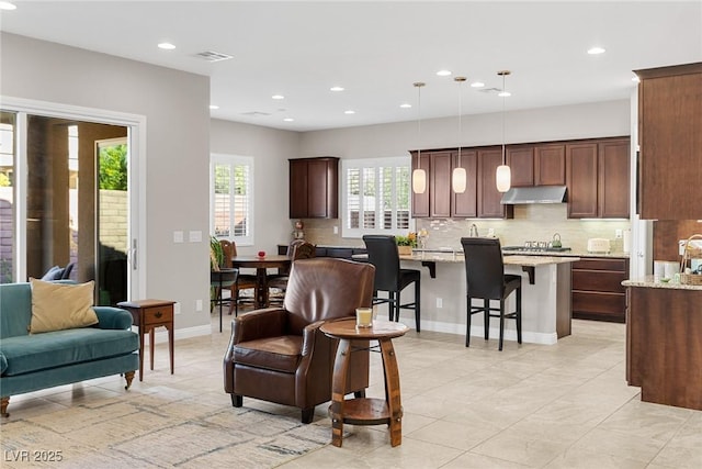 kitchen featuring decorative light fixtures, a kitchen island, decorative backsplash, a kitchen breakfast bar, and light stone counters