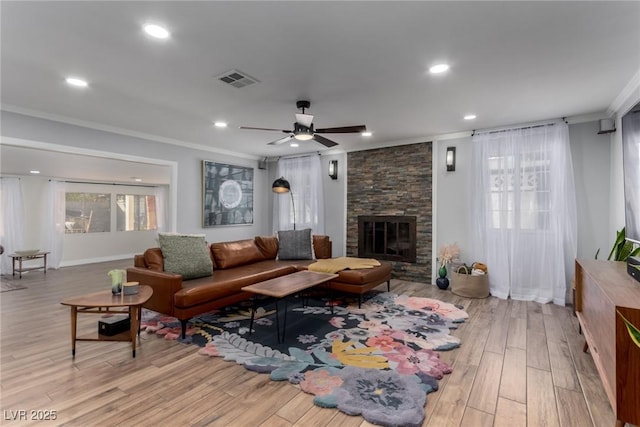 living room featuring ceiling fan, ornamental molding, light hardwood / wood-style floors, and a stone fireplace