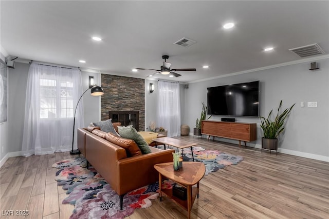 living room featuring ceiling fan, a fireplace, crown molding, and light hardwood / wood-style flooring