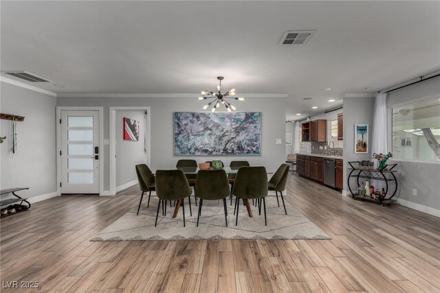 dining room with sink, light hardwood / wood-style flooring, crown molding, and an inviting chandelier