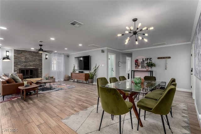 dining area with light wood-type flooring, ceiling fan with notable chandelier, a stone fireplace, and ornamental molding