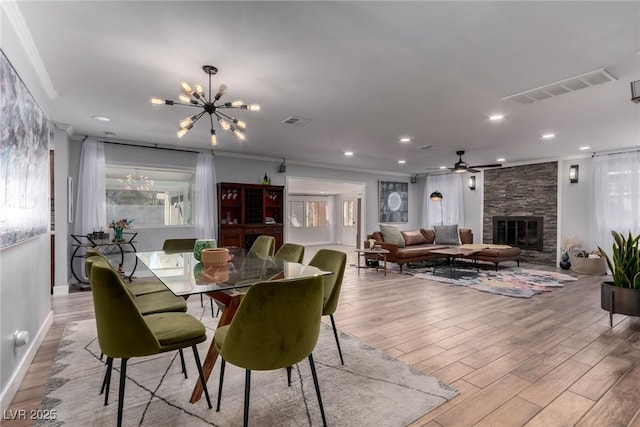 dining area featuring light wood-type flooring, ceiling fan with notable chandelier, crown molding, and a fireplace