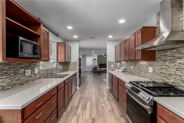 kitchen with appliances with stainless steel finishes, wall chimney exhaust hood, decorative backsplash, sink, and light hardwood / wood-style floors