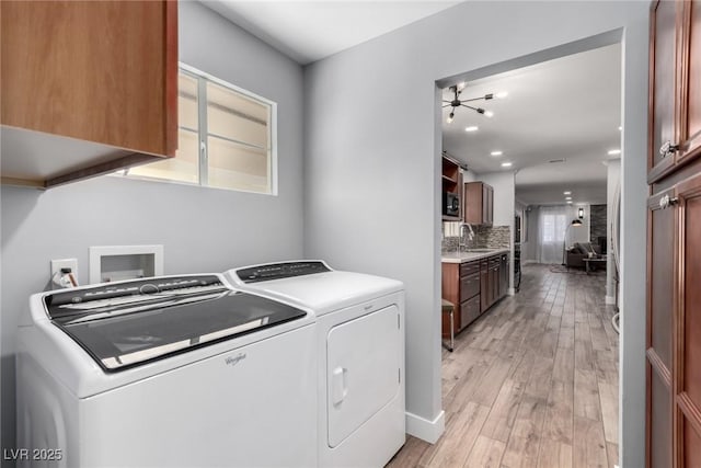 clothes washing area with cabinets, sink, independent washer and dryer, and light wood-type flooring