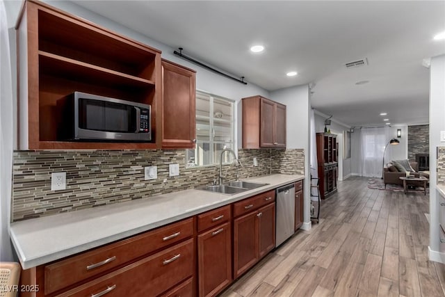 kitchen with backsplash, a fireplace, sink, light wood-type flooring, and appliances with stainless steel finishes