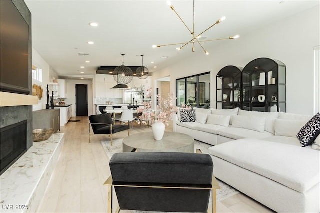 living room featuring a premium fireplace, a chandelier, and light hardwood / wood-style floors