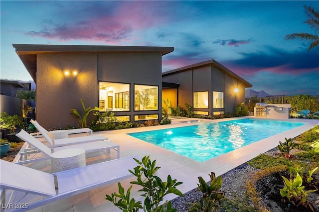 pool at dusk featuring exterior kitchen and a patio