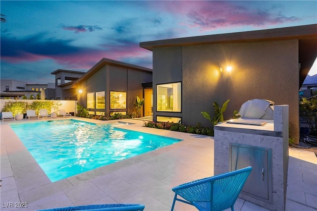 pool at dusk featuring a patio area and an outdoor kitchen