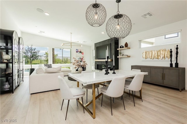 dining area with vaulted ceiling, light hardwood / wood-style flooring, and an inviting chandelier