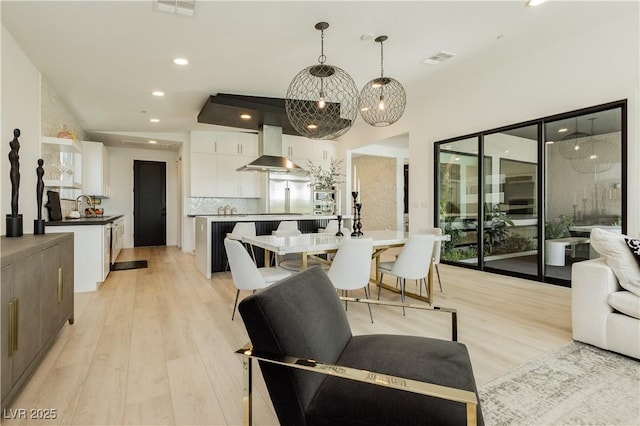 kitchen with pendant lighting, exhaust hood, white cabinetry, decorative backsplash, and light hardwood / wood-style flooring