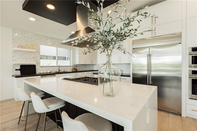 kitchen featuring island range hood, appliances with stainless steel finishes, a spacious island, light wood-type flooring, and sink