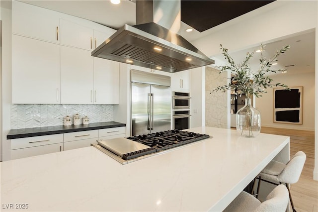 kitchen featuring white cabinets, backsplash, appliances with stainless steel finishes, and island exhaust hood