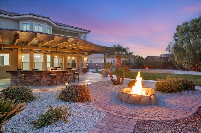 patio terrace at dusk featuring an outdoor fire pit and a bar