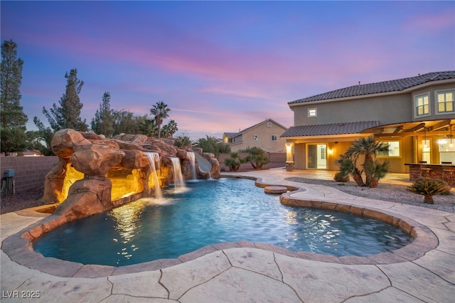 pool at dusk with pool water feature and a patio area